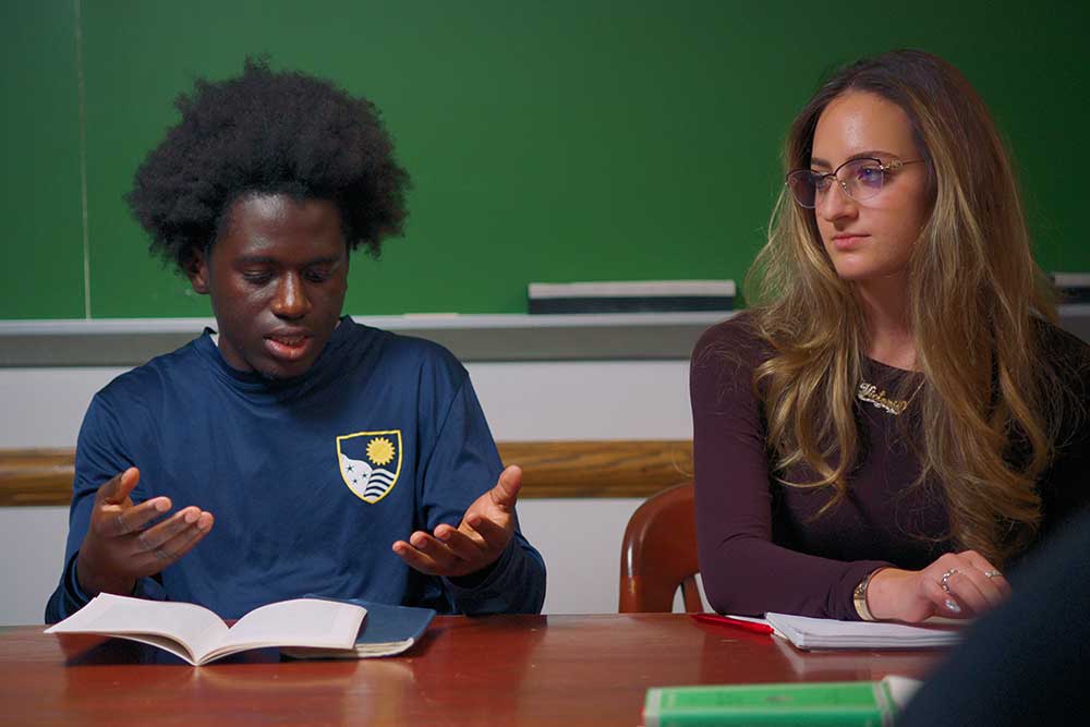Two students in class. One is talking as the other looks on.